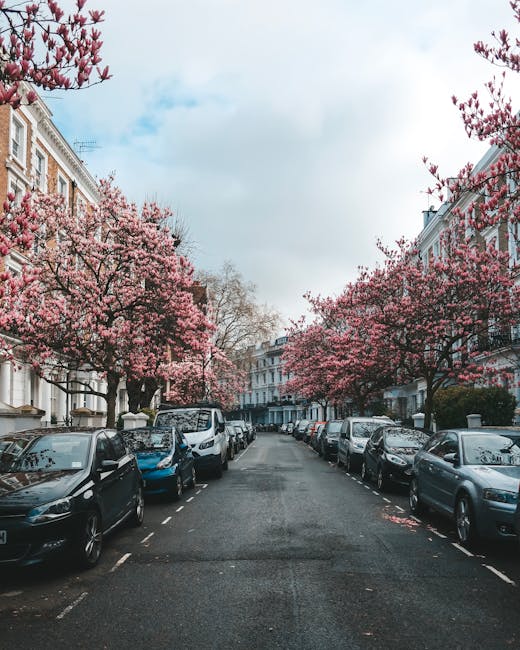 A long, narrow exterior corridor of a townhouse with white painted walls and multiple white columns along the perimeter. Potted plants with yellow flowers are placed on a ledge along the left side, an